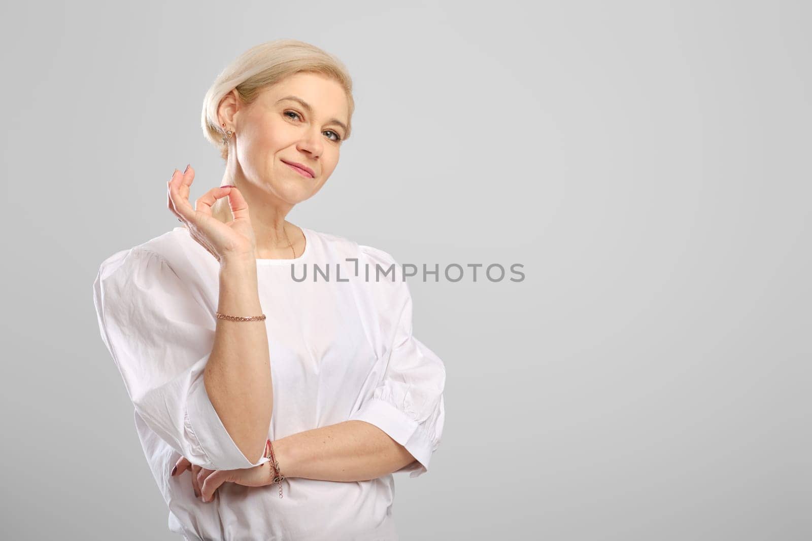 Studio portrait of middle age woman showing ok gesture. (photo with place for text)