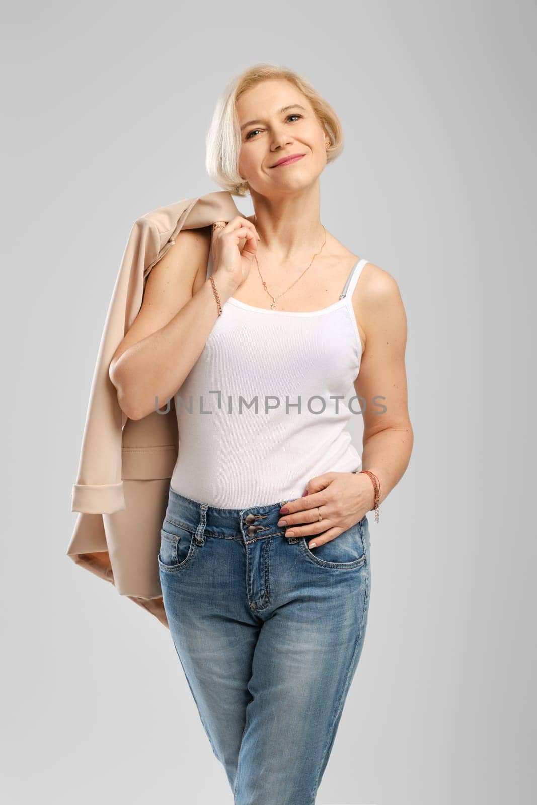 Studio portrait of successful middle age woman, self-confident holding beige jacket over the shoulder in studio