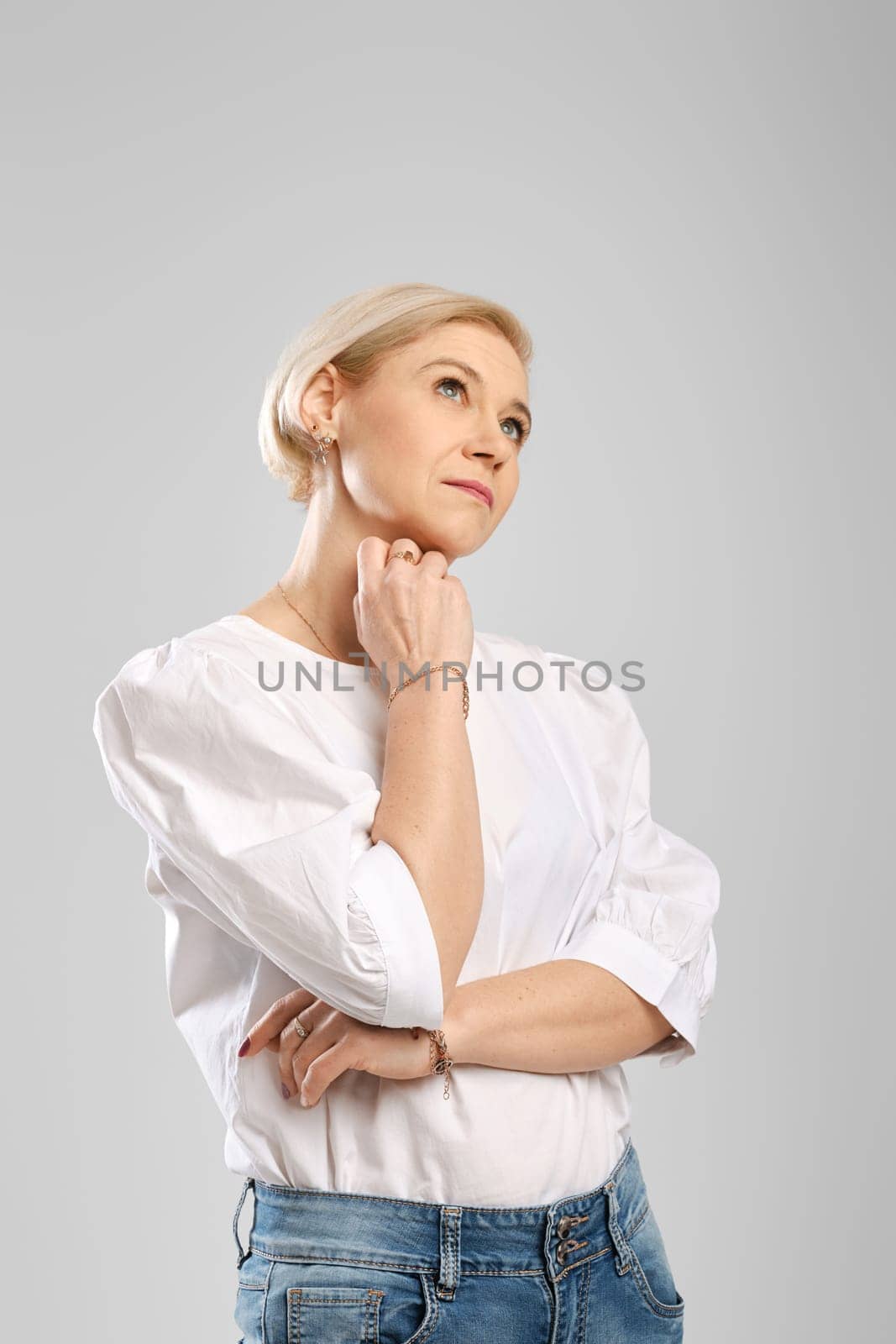 Studio portrait of middle age woman, propping chin, looking up and thinking