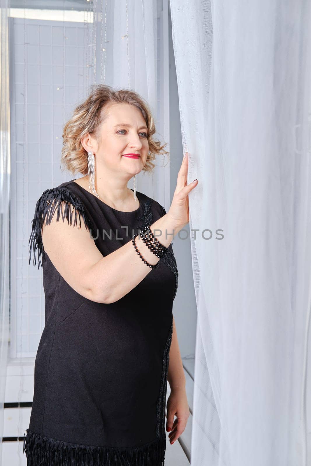 Middle age woman woman pulls back the curtain and looks out the window