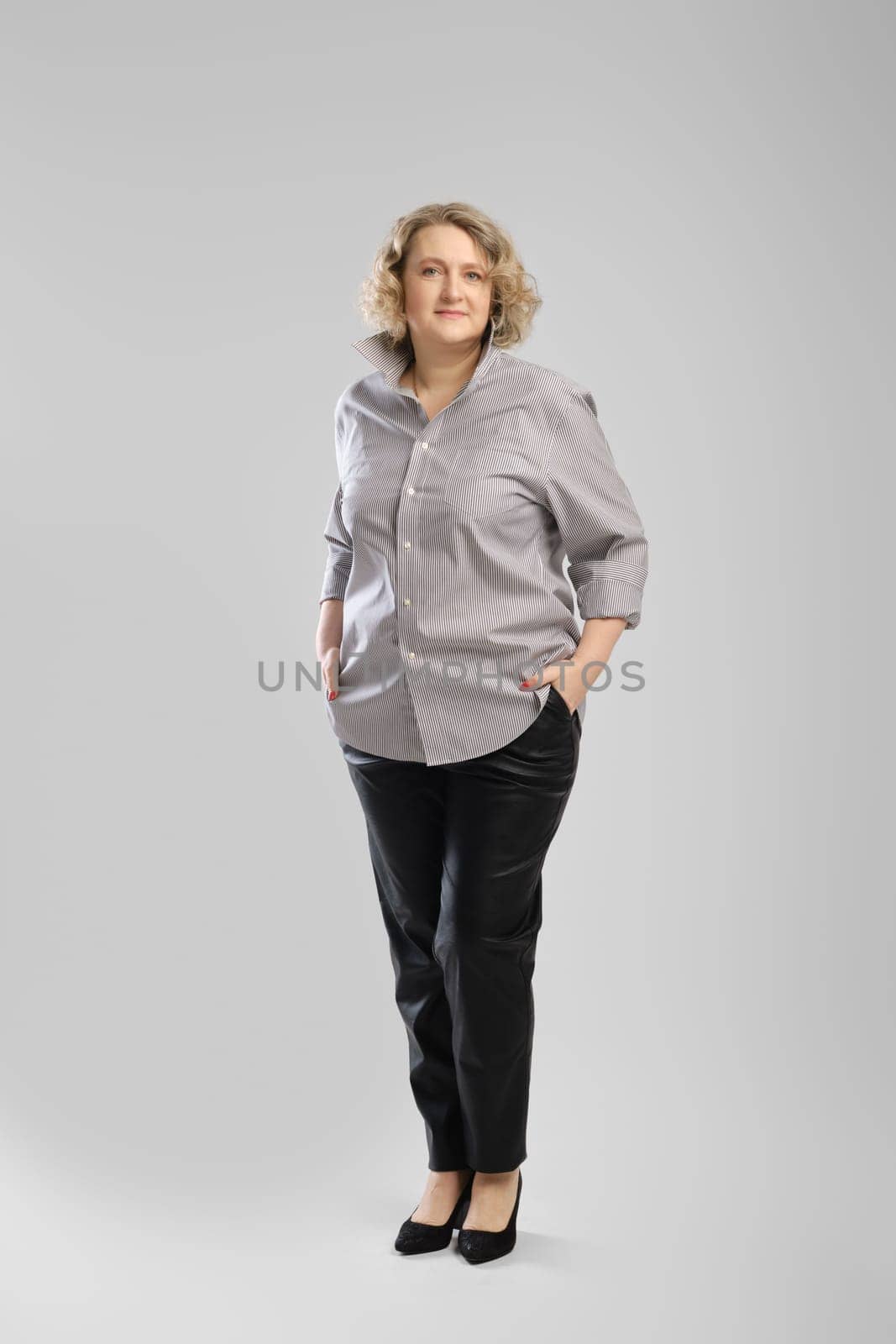 Full body casual portrait of senior woman in grey shirt and trousers over grey studio background