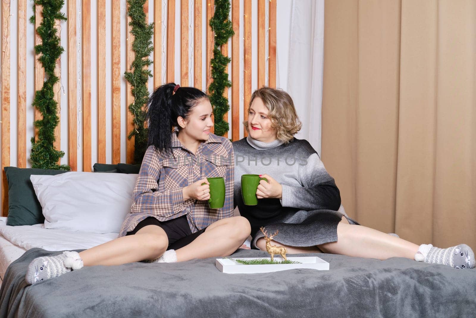 Elder mother and daughter sitting on bed, share impressions, talking