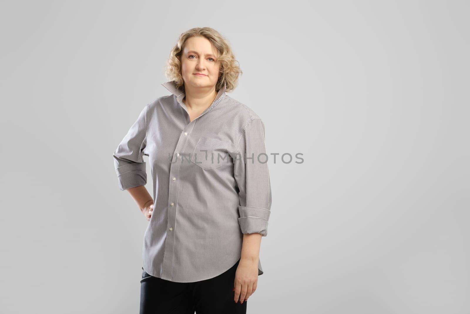 Casual portrait of senior woman in grey shirt and trousers over grey studio background