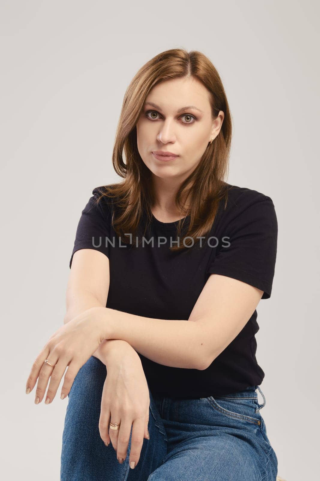 Portrait of young woman in black t shirt and jeans posing over grey background