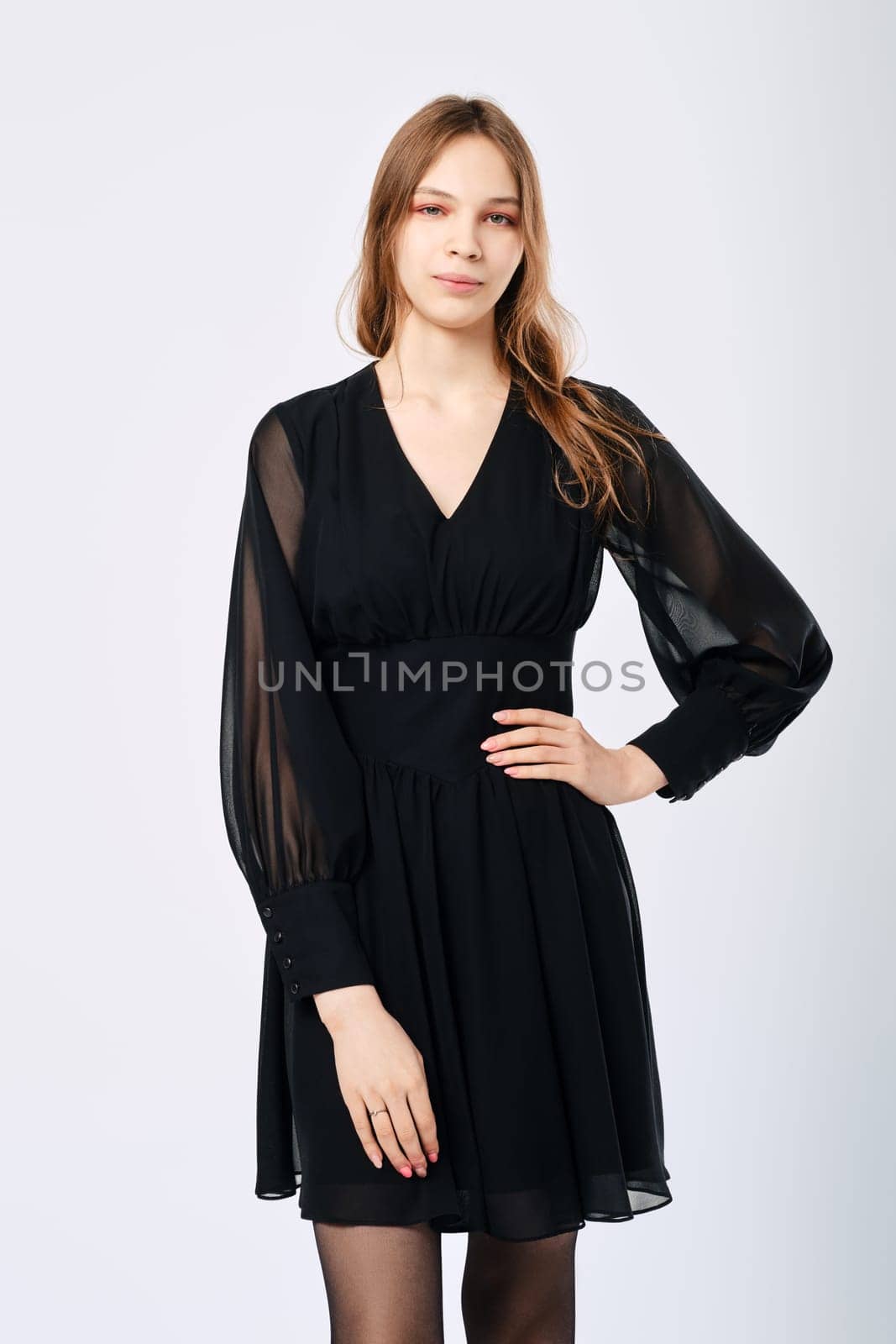Young woman posing in studio in little black dress with one arm on waist