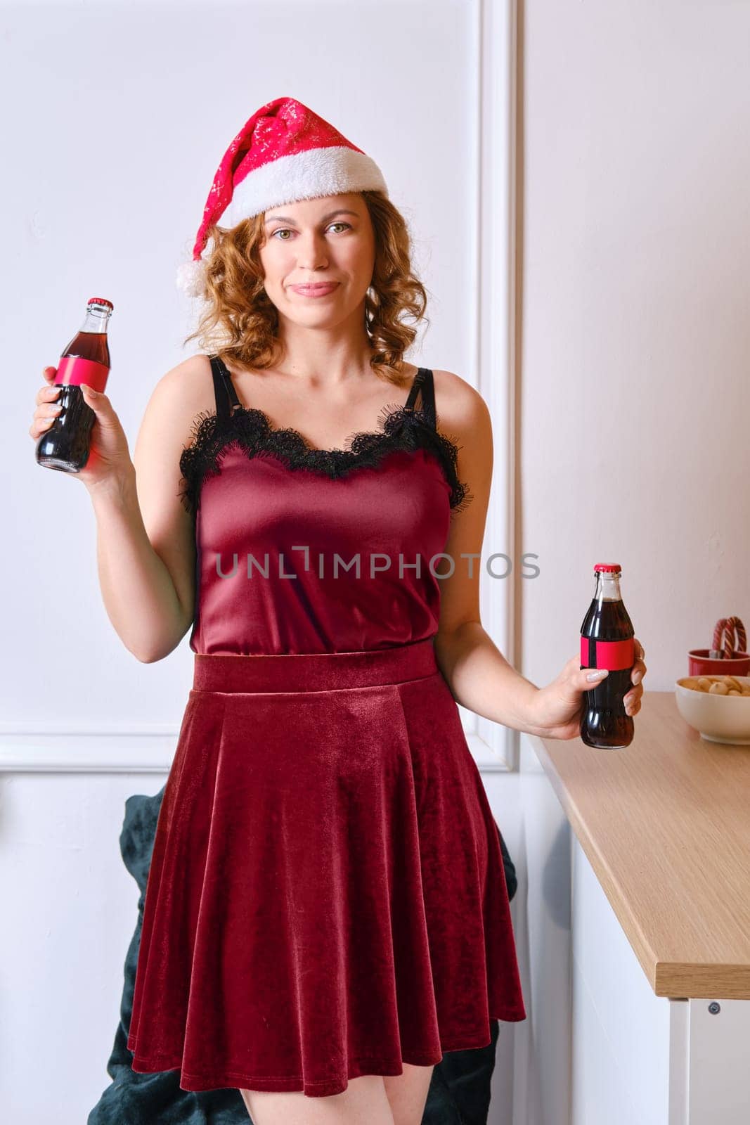 Red hair woman in christmas cap holds two bottles of cola in hands