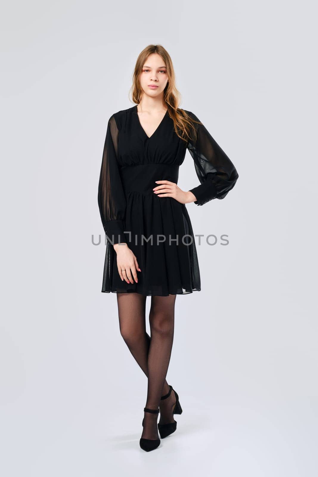 Young woman posing in studio in little black dress with one arm on waist