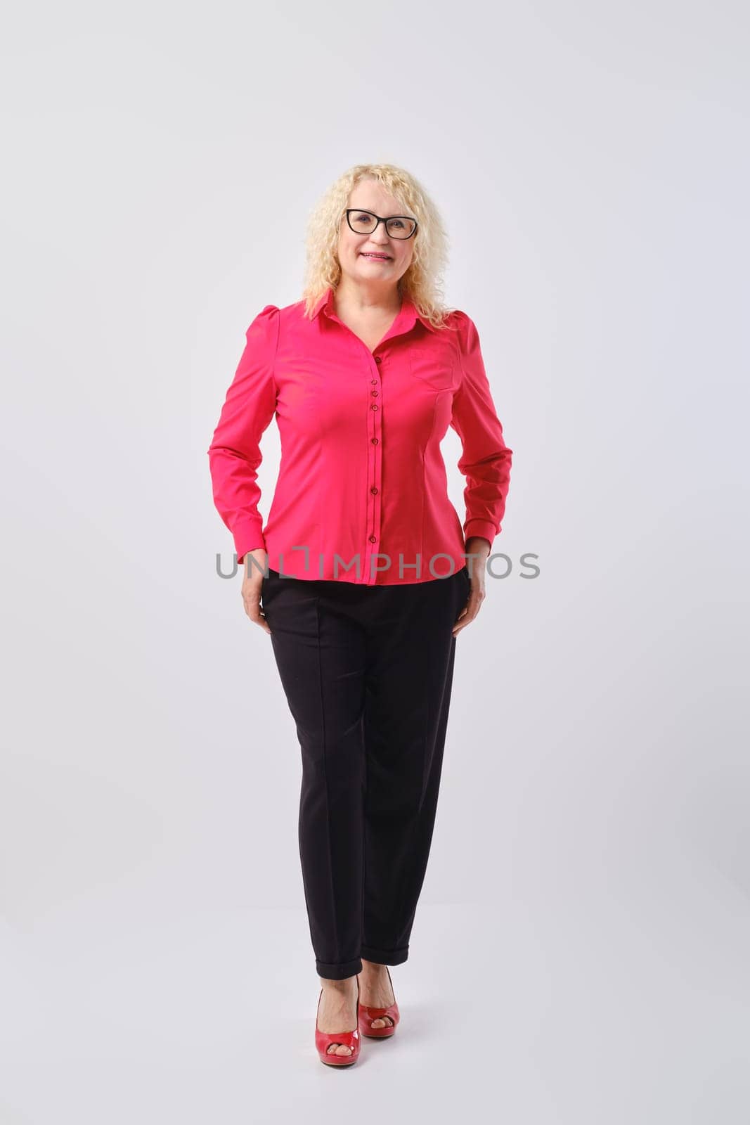 Middle aged woman in red shirt and black trousers posing over grey background