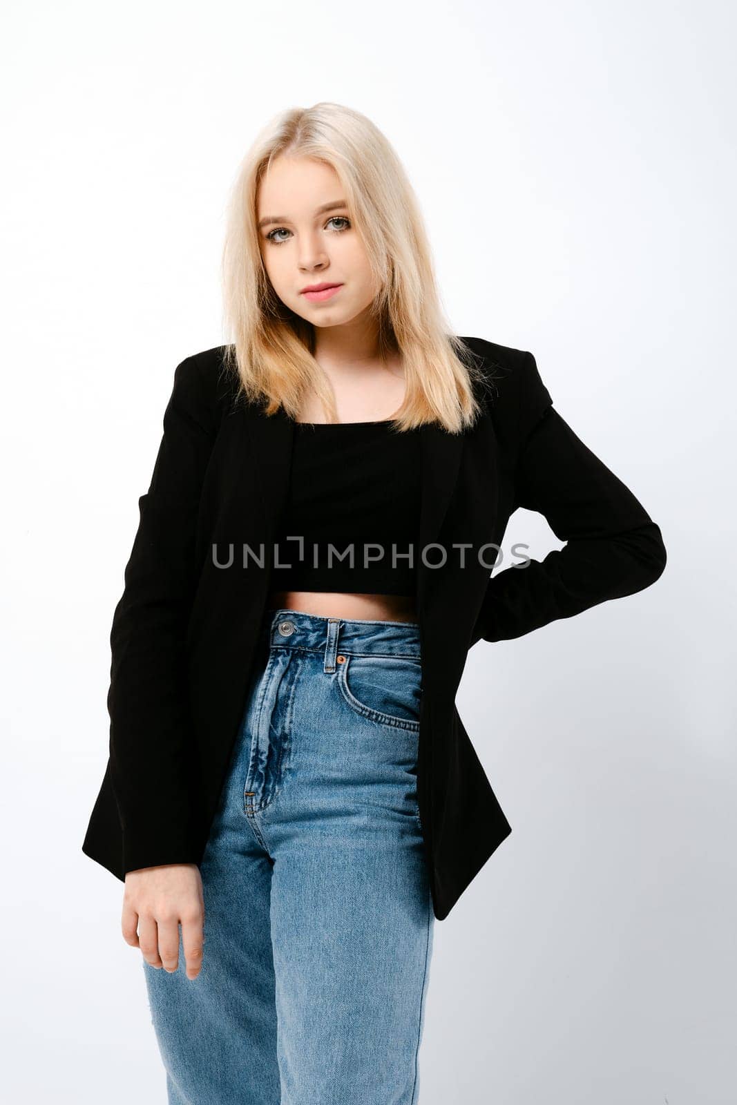 Blonde girl in tank top, jacket and jeans posing over bright grey background