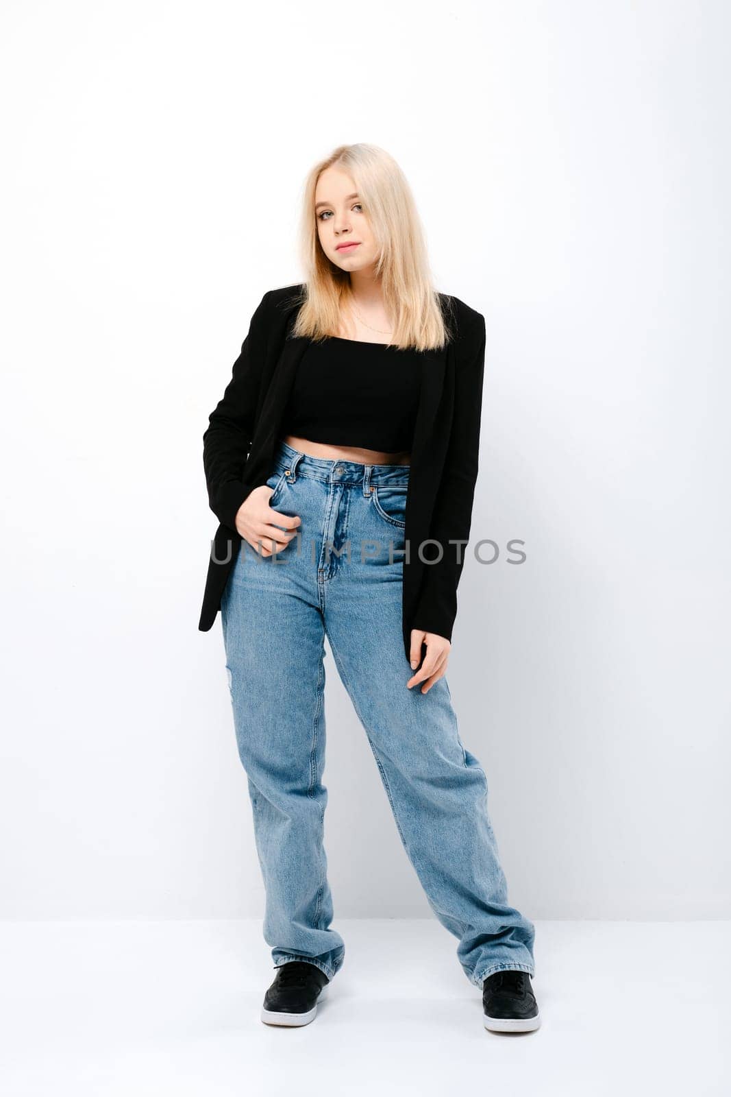 Blonde girl in tank black top, jacket and jeans posing