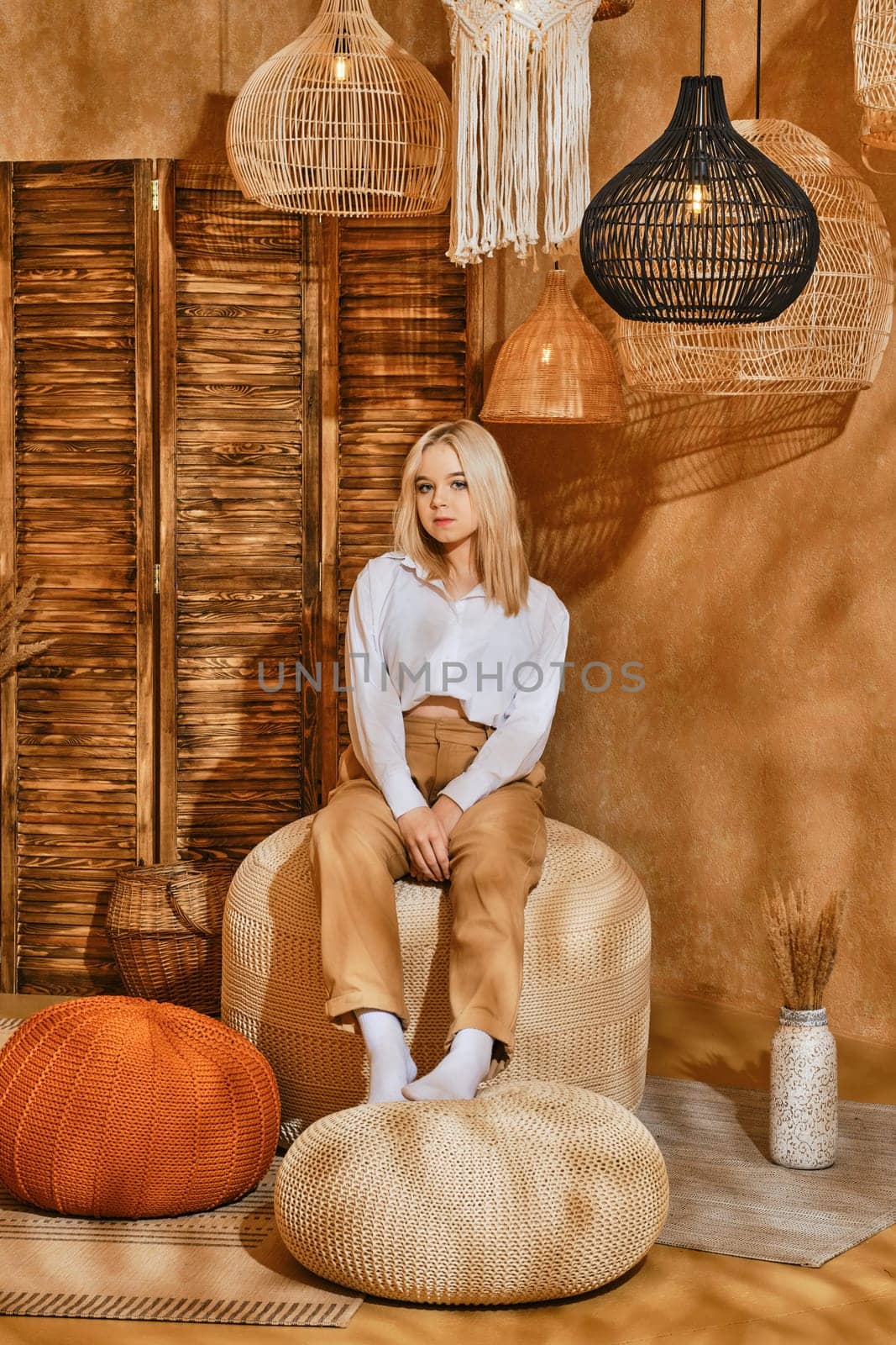 Teenager girl in white shirt and brownish trousers sitting on padded stool