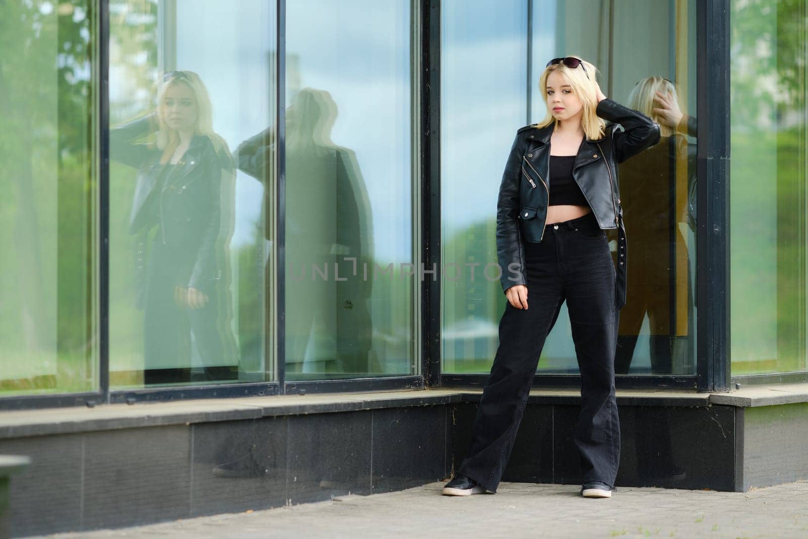 Young teenager girl in black clothes near glass wall of the building