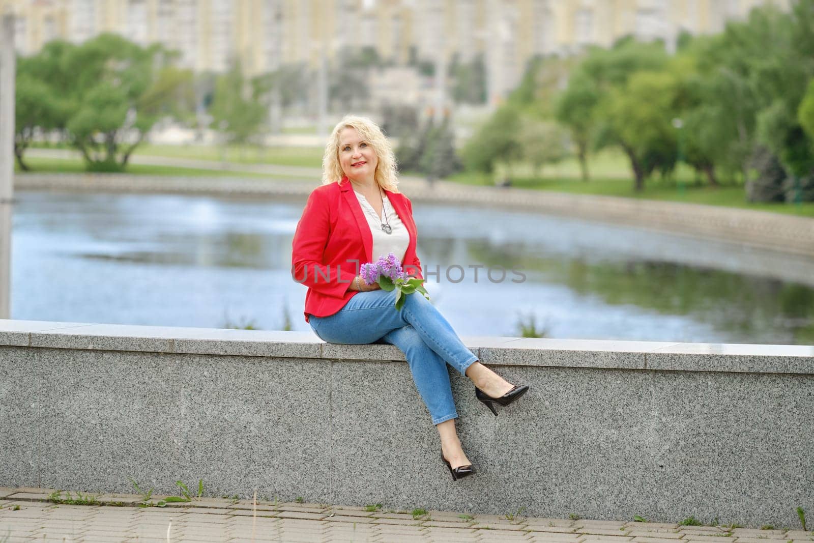 Positive middle-aged woman is sitting on the embankment in a city park