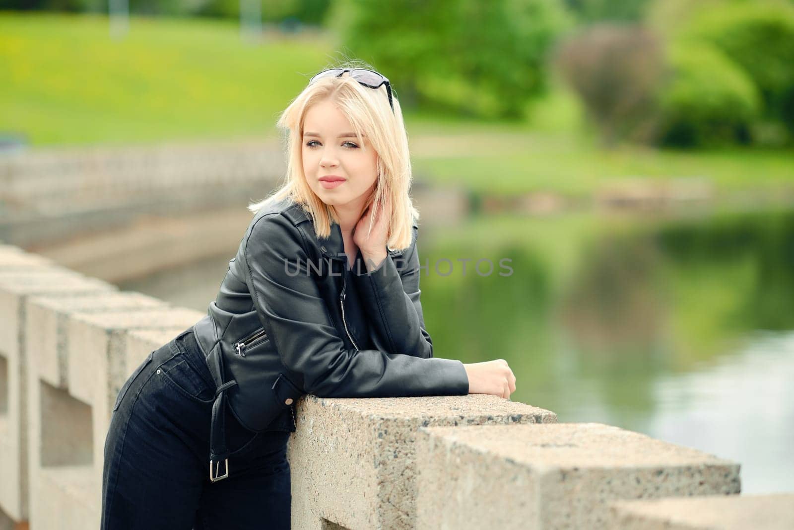 Portrait of cute teenager girl in black jeans, tank top and leather jacket on river bank
