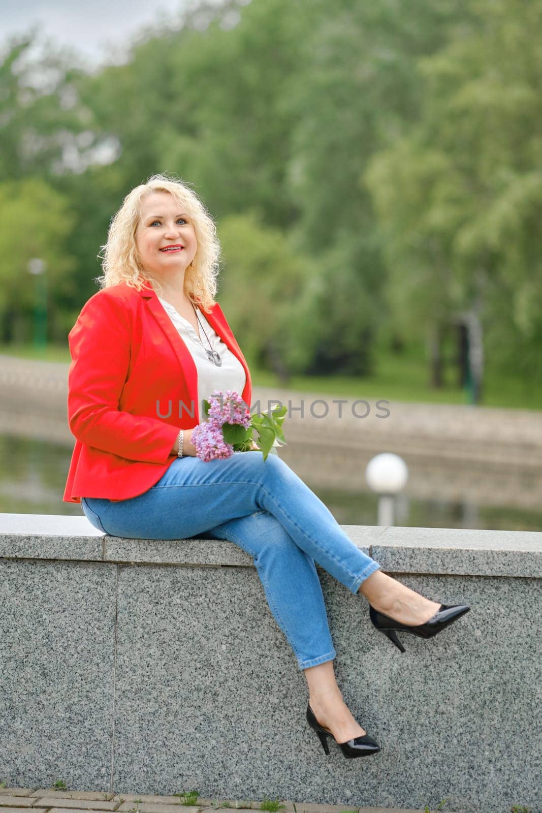 Happy middle-aged woman sits on the embankment in a city park