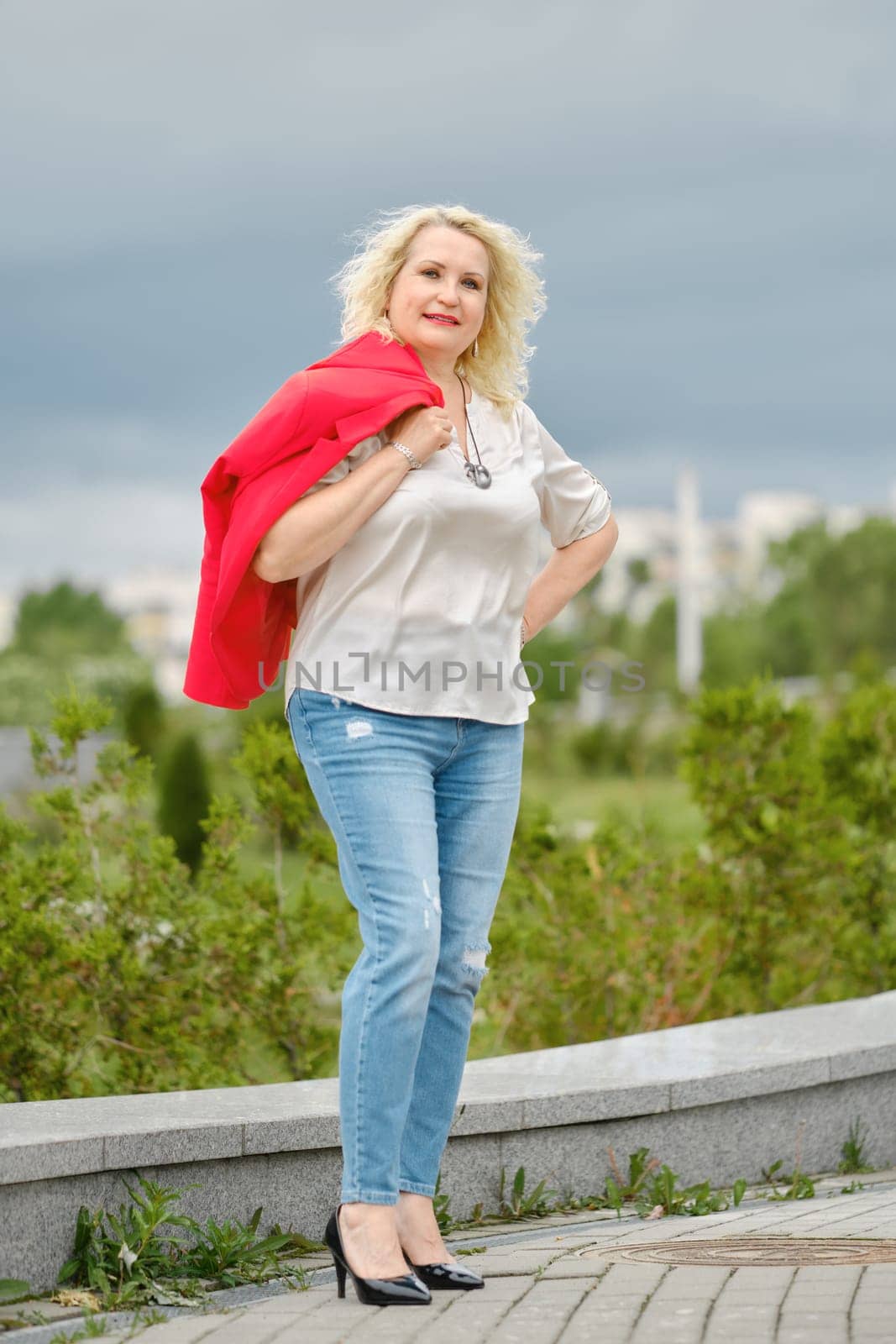 Cheerful senior woman walks in the city, she slung her jacket over her shoulder