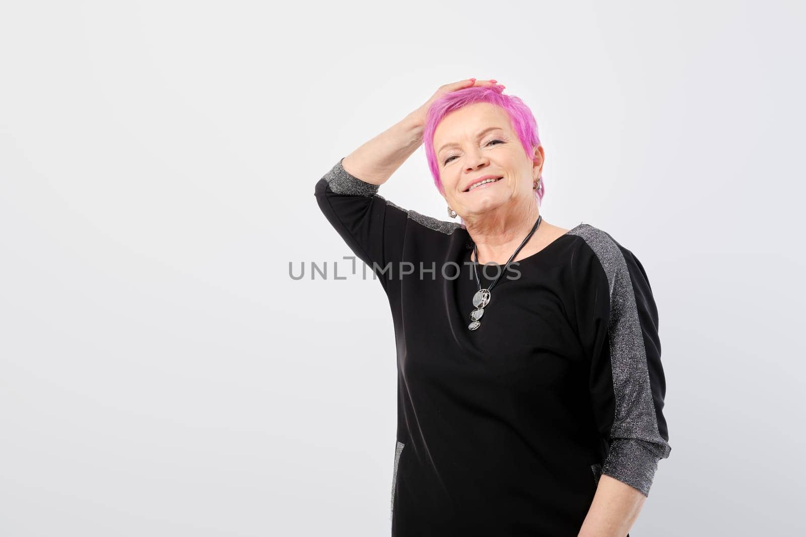 Happy old woman runs her hand through her short pink hair over white background