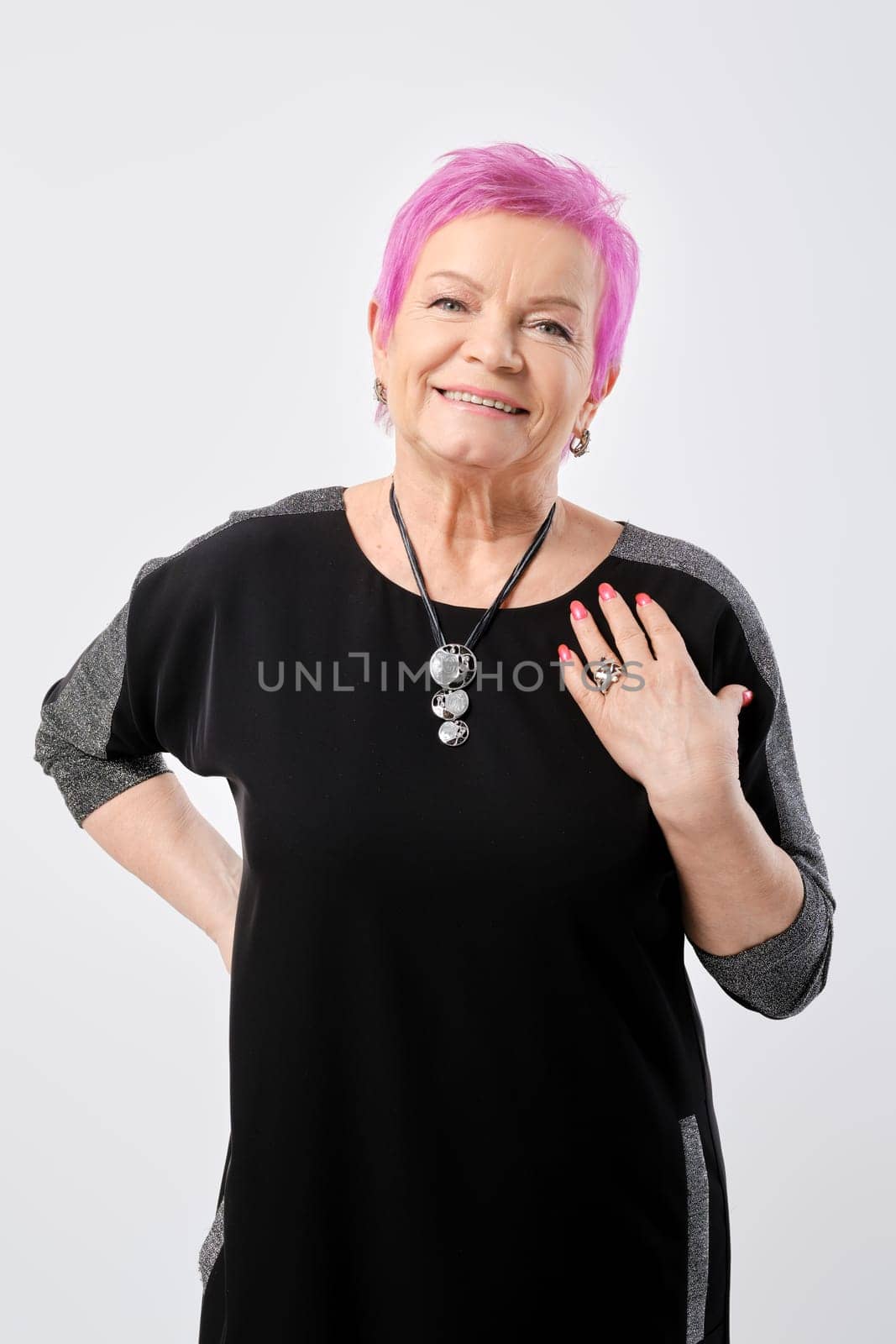 Positive old woman with short pink hair explains and gestures something in white studio
