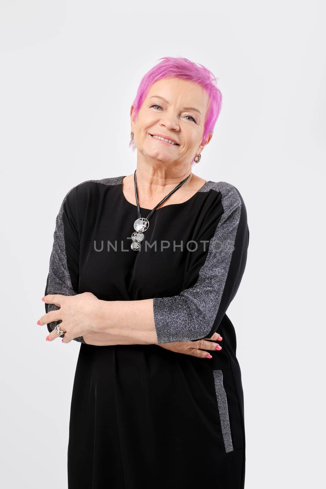 Smiling old woman with short pink hair keeps hands crossed. Positive emotion concept.