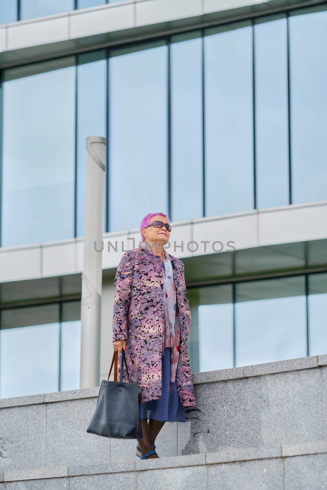 Old woman with pink hair in cashmere coat and hand bag walking