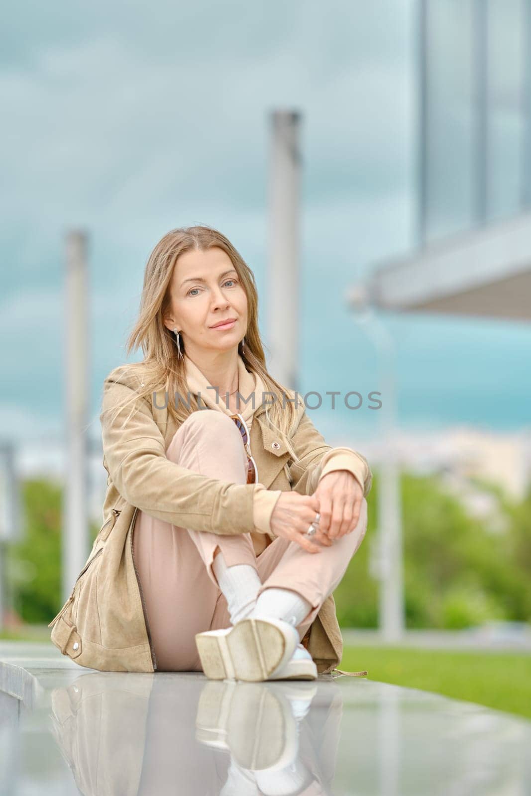 Portrait of pensive middle aged woman sitting on marble railing with dramatic sky on background