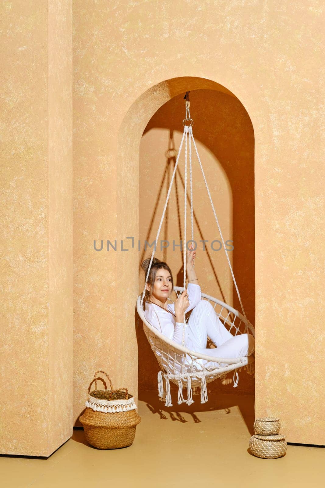 Active middle aged woman sits in profile on swing in white clothes in hot sunny day