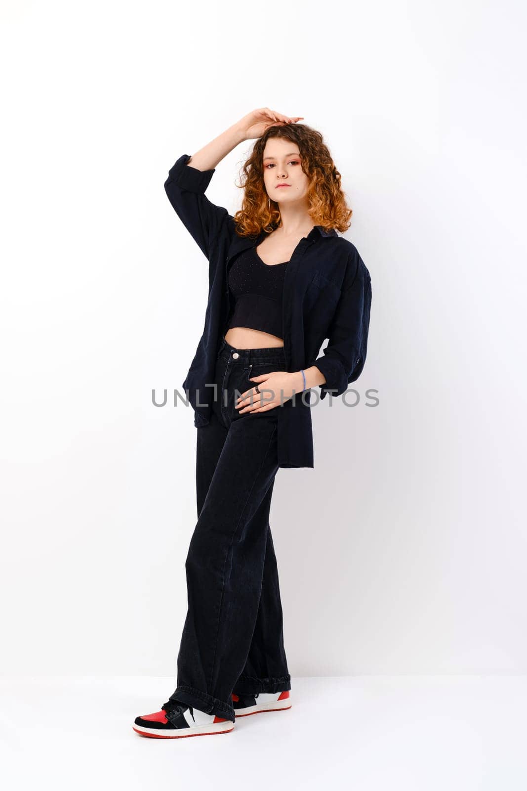Young teenager model in black trousers and shirt posing over white background