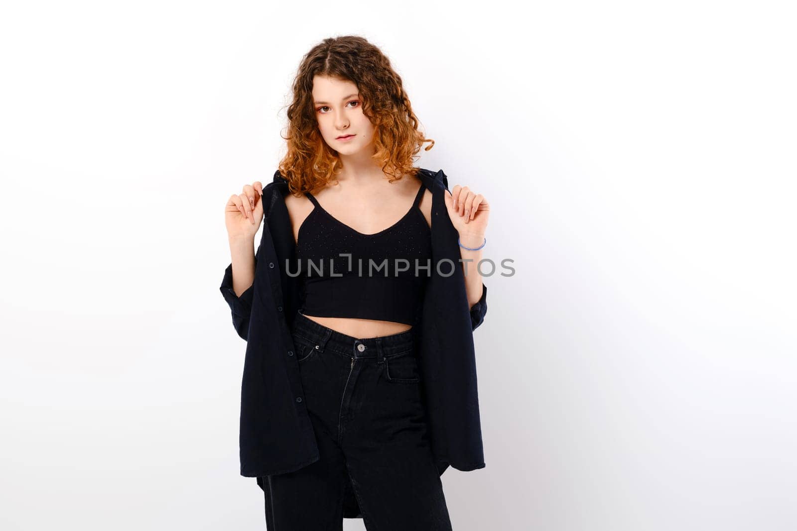 Serene caucasian teenage girl in casual clothing with colored ends of hair holds edges of black shirt over white studio background