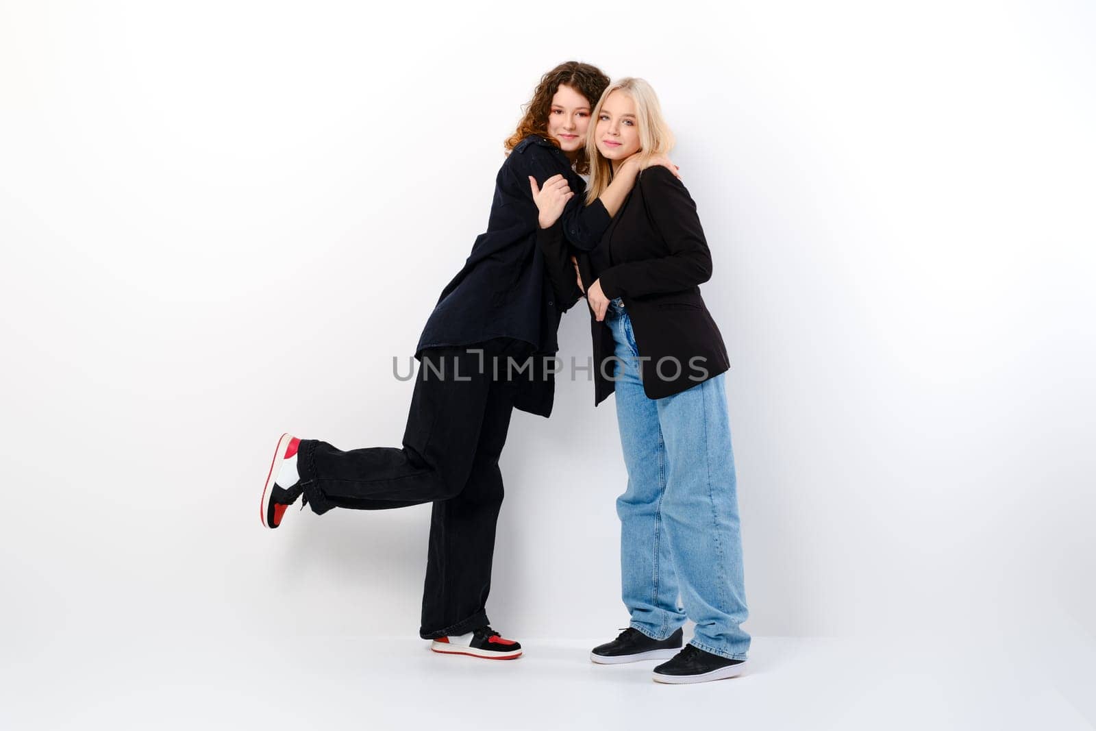 Two teen girls lean on each other over white studio background