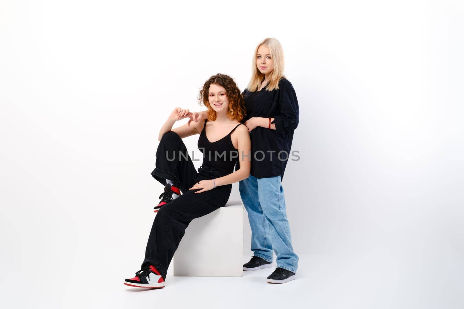 Two positive and funny teen girls together over white studio background