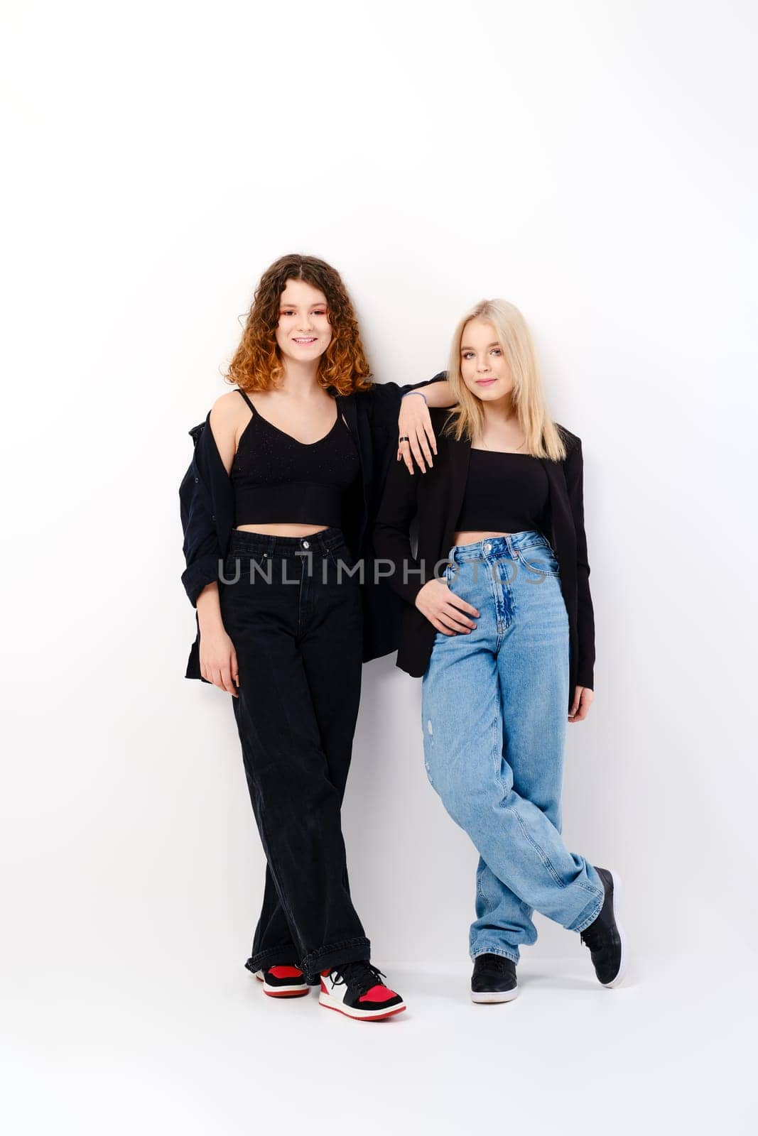 Two teen girls lean on each other over white studio background