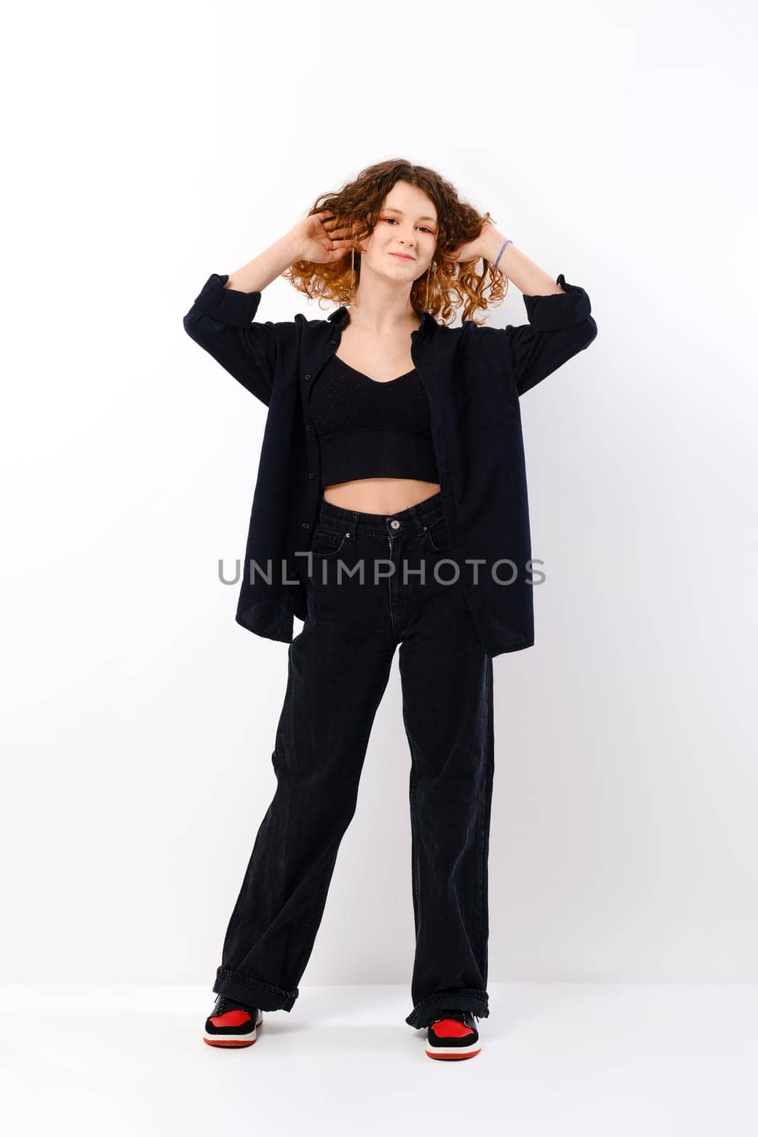 Funny smiling teenager girl in black clothes touching colored curly hair