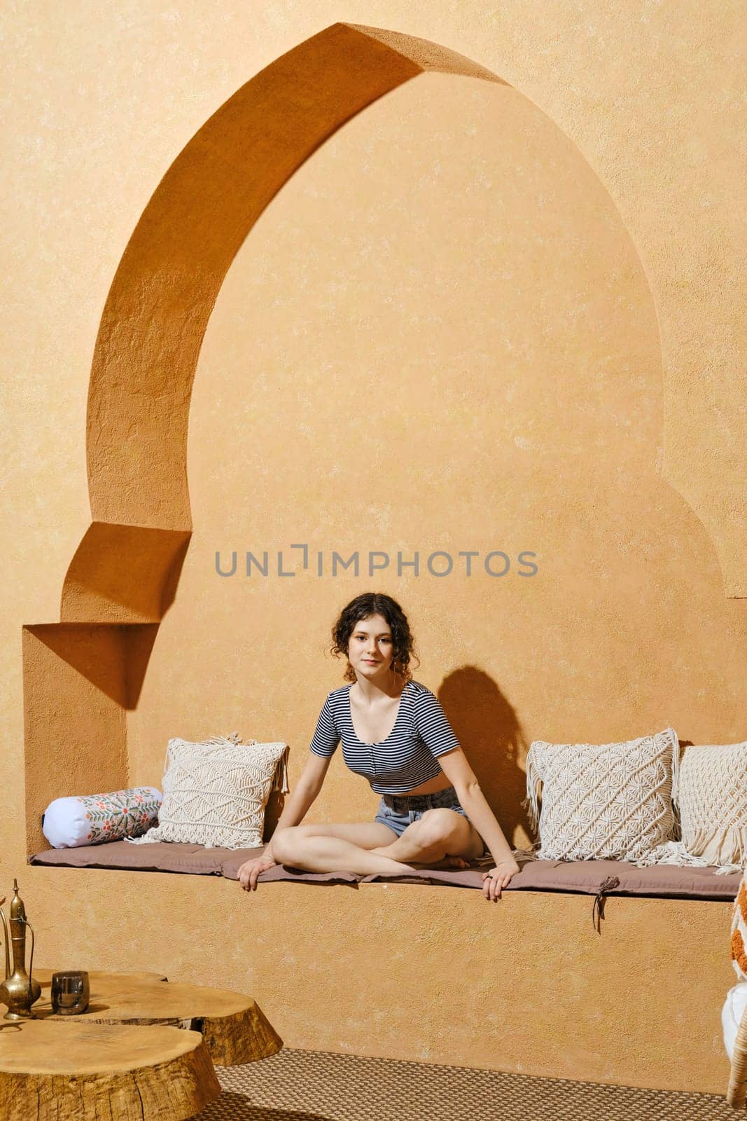 Teenager girl sits cross-legged on stone bench in sunny day