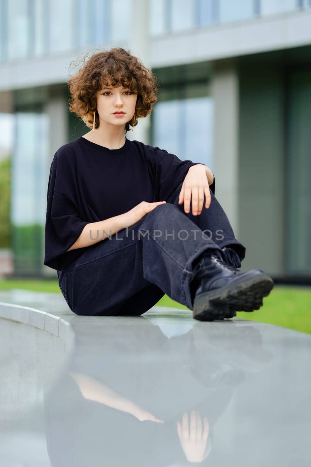 Girl in wide black jeans, shirt and rough boots sits on marble railing