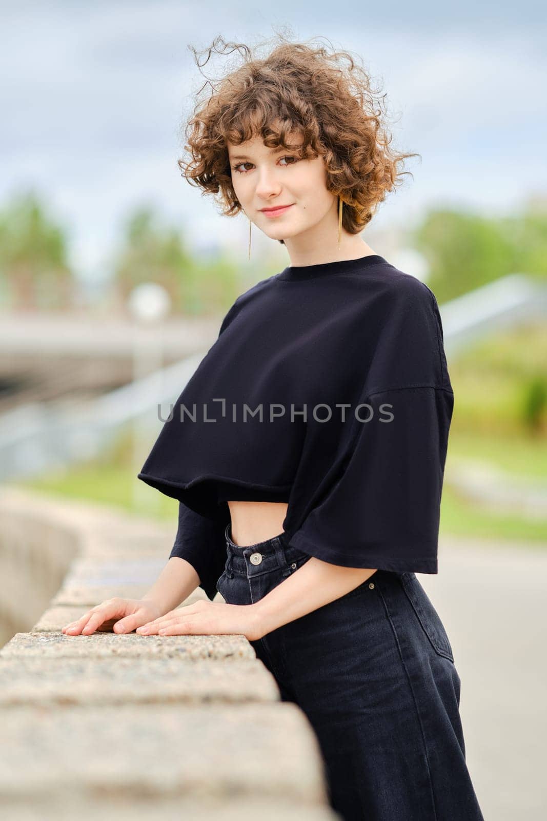 Teenager girl in black clothes leaning on stone parapet in city park