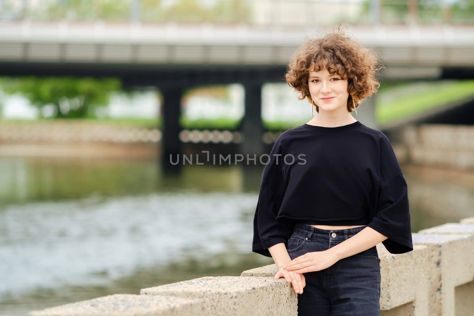 Portrait of smiling teenager girl in black jeans and t-shirt near the river