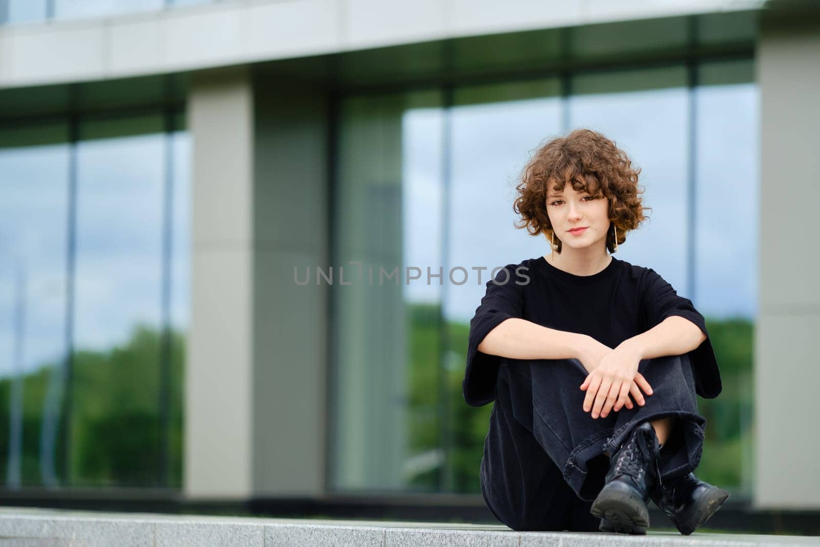 Teenager girl in wide black jeans, t-shirt and rough boots sits on marble railing