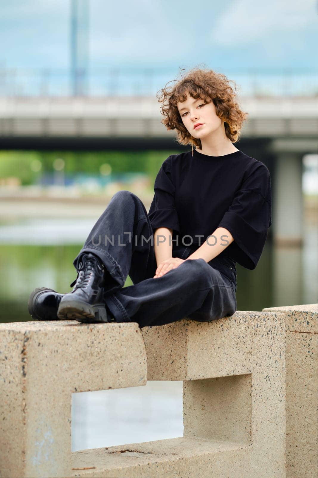 Portrait of smiling teenager girl in black jeans, t-shirt and rough boots near the river