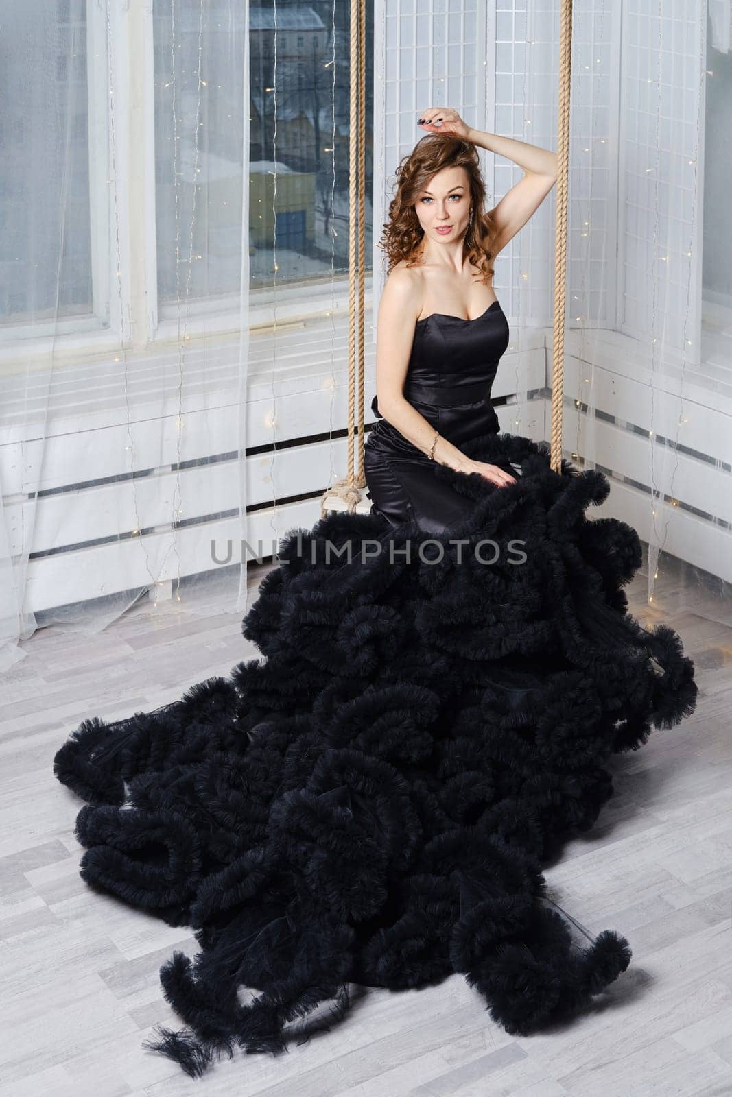 Gorgeous woman in a luxurious puffy black dress sits on a swing
