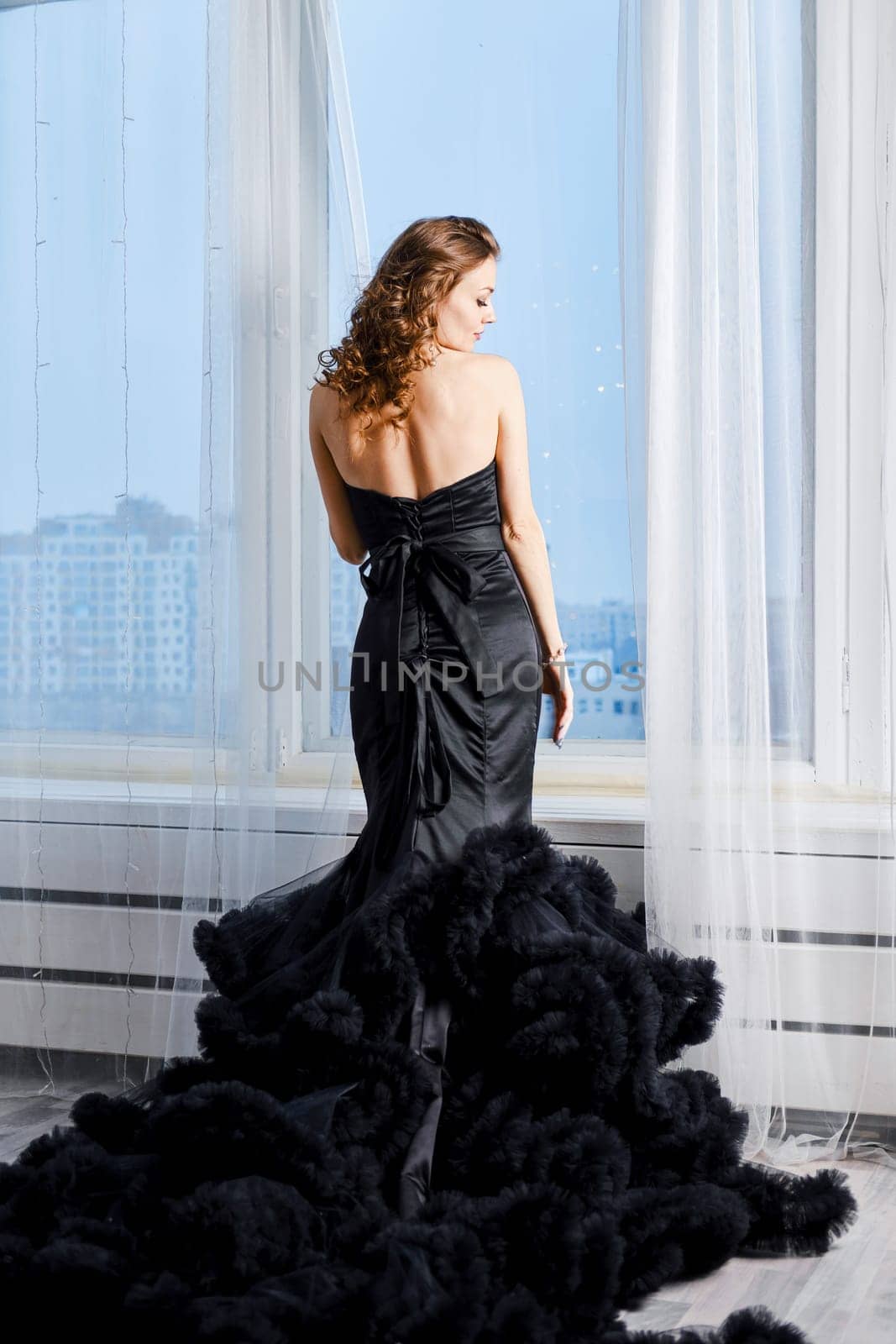 Rear view of orgeous young woman in evening dress looking through the window