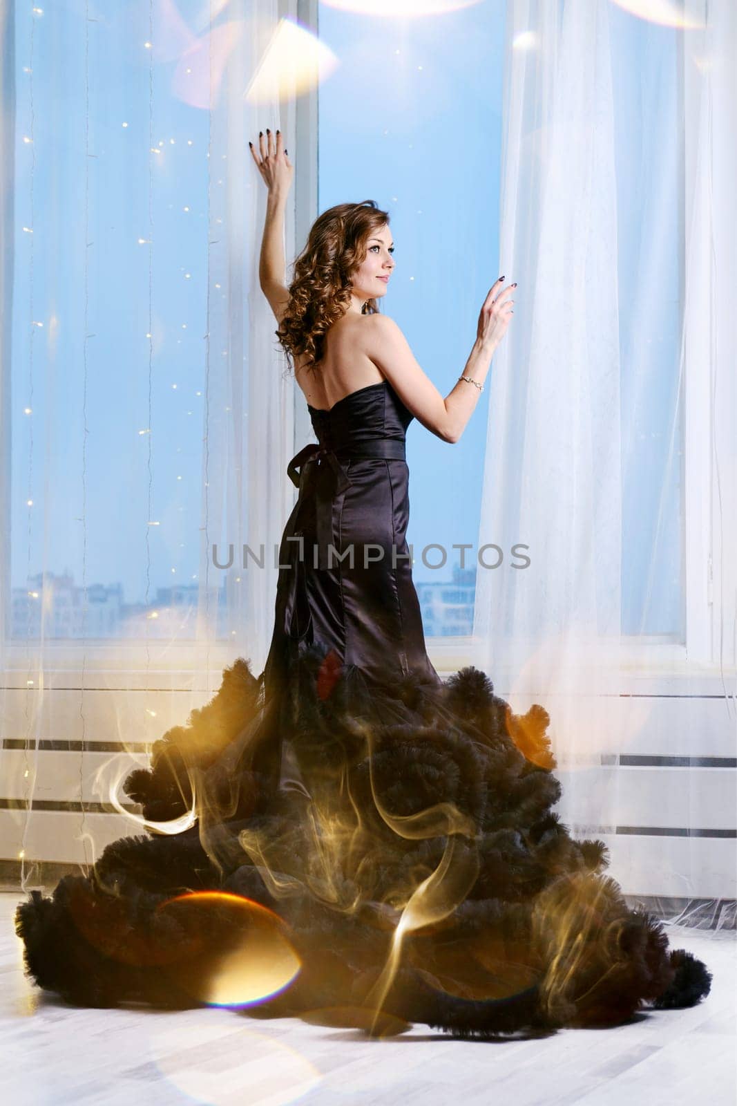 Gorgeous young woman in evening dress looking through the window