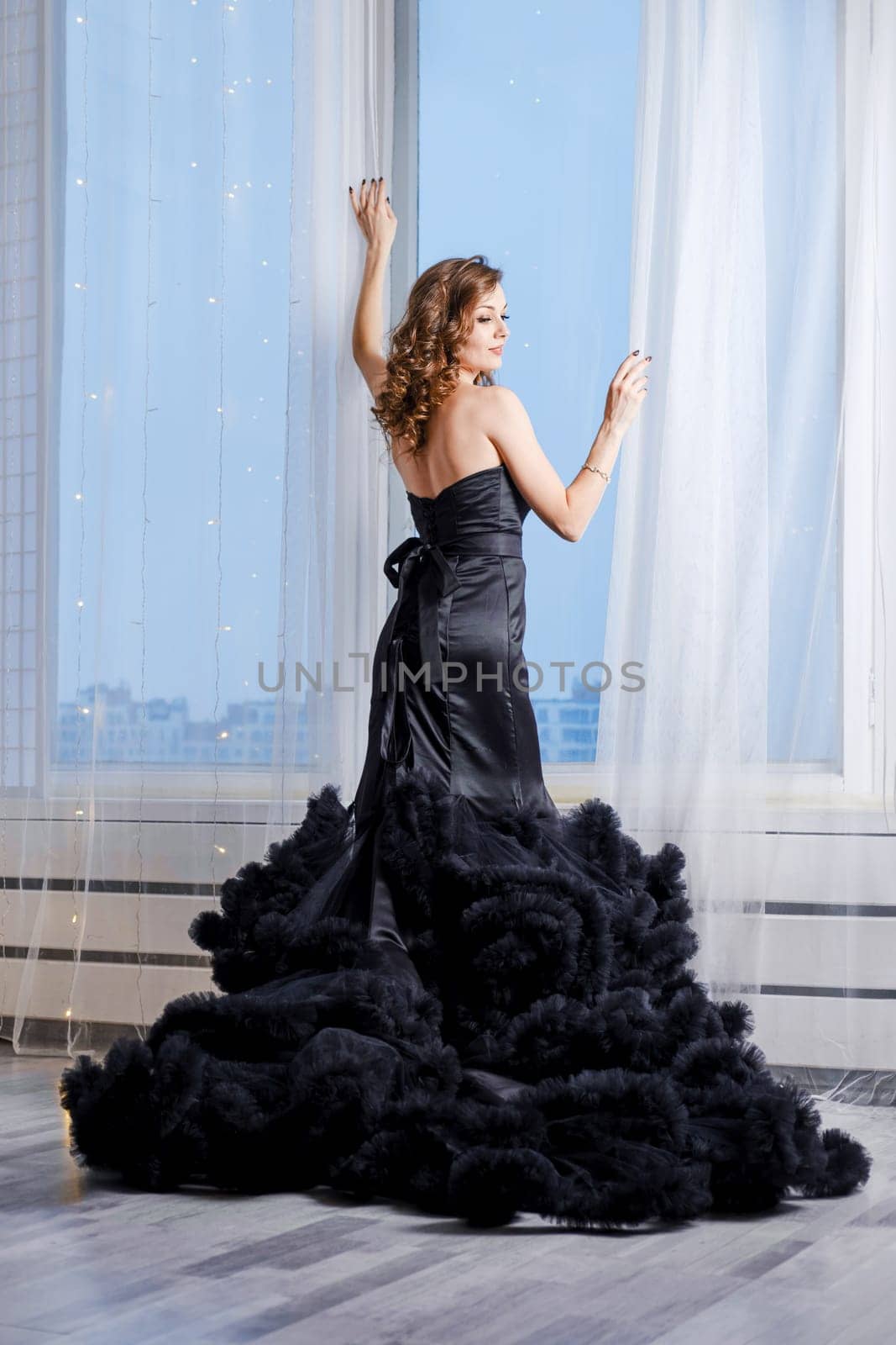Gorgeous young woman in evening dress looking standing by the window