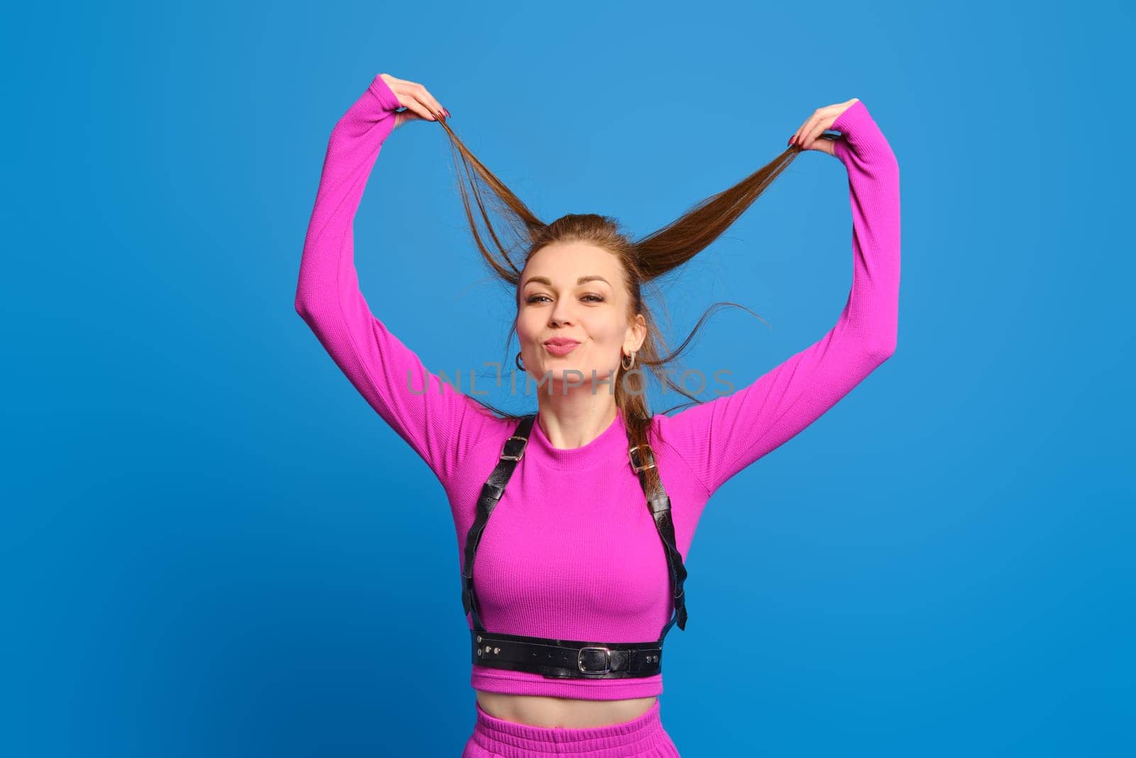 Happy woman in purple knitted suit playing with hair over blue studio background