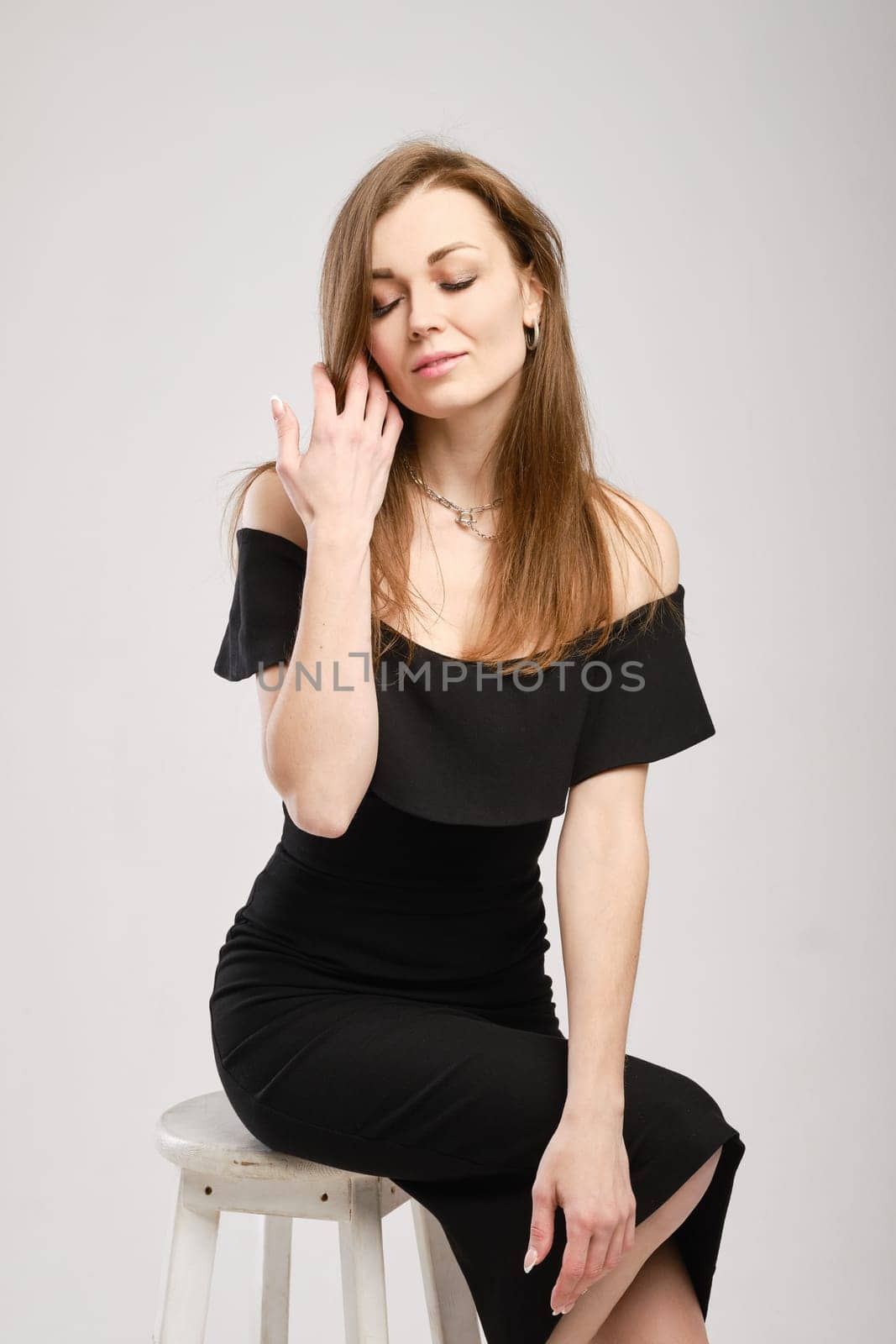 Studio portrait of pretty young woman in black dress on tall wooden chair