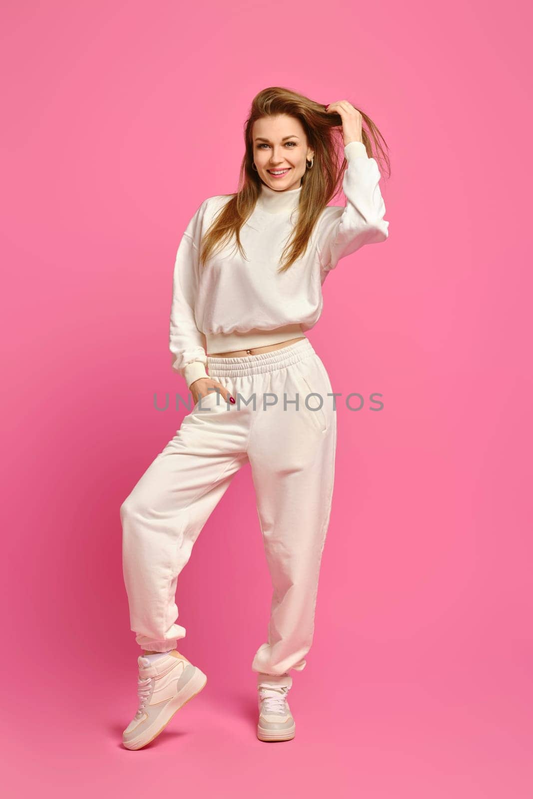 Sporty woman in white fleece sweatshirt and sweatpants posing over bright pink studio background