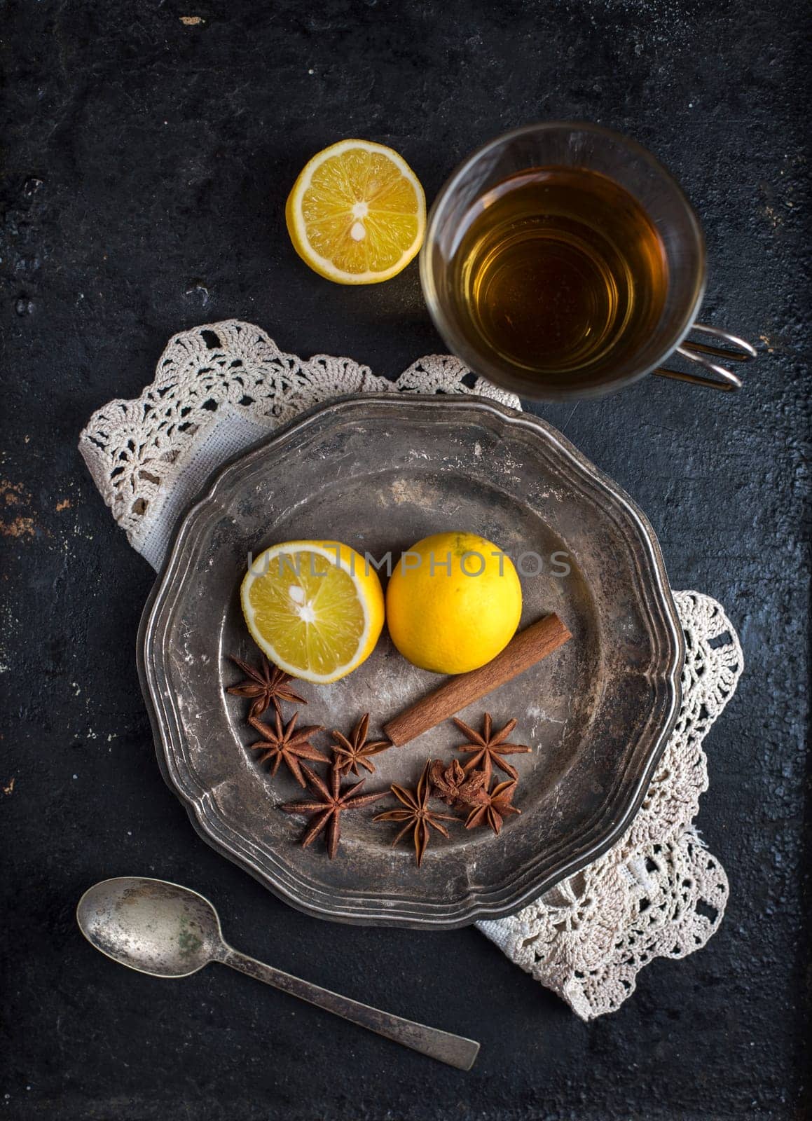 Top view of vintage tea set with aromas and lemon on rustic black background. Food and drink still life. Cup of hot beverage with anise, cinnamon and lemon.