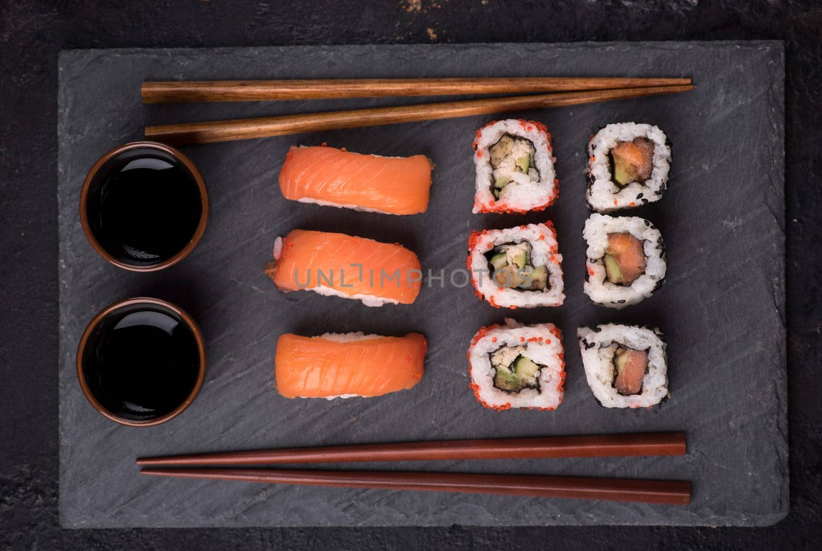 Sushi rolls set with salmon and tuna fish on black sushi board from above. Top view of traditional japanese cuisine. Asian food on black stone slate with chopsticks.