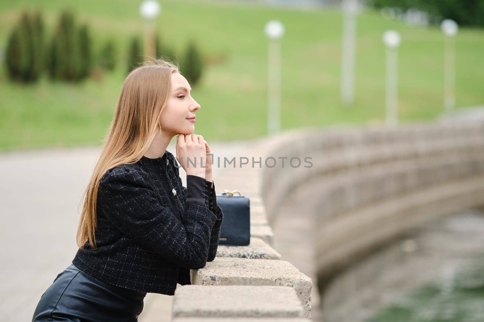 Cute woman leans against the railing and looks thoughtfully at the river