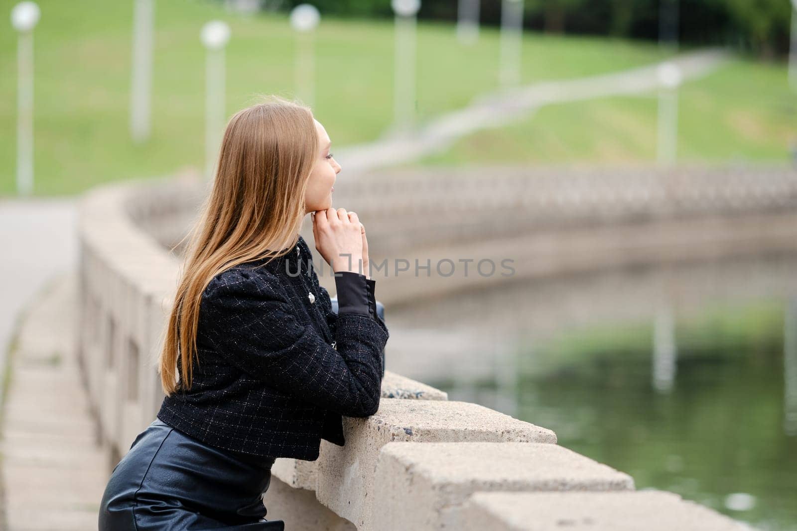 Young woman leans against the railing and looks thoughtfully at the river