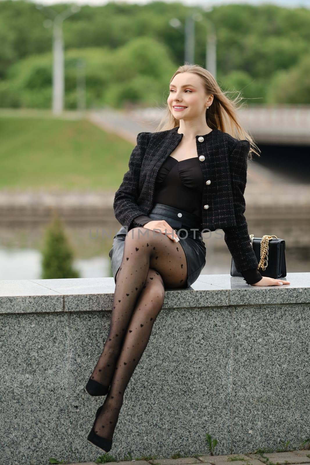 Pretty young woman sitting on river bank in city park near her office